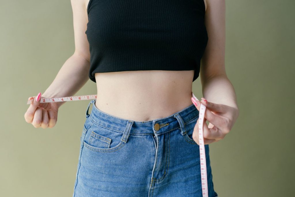 A woman in denim and crop top using measuring tape for waist check.