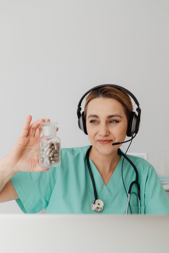 Female doctor with headset holding pill bottle. Telemedicine concept.